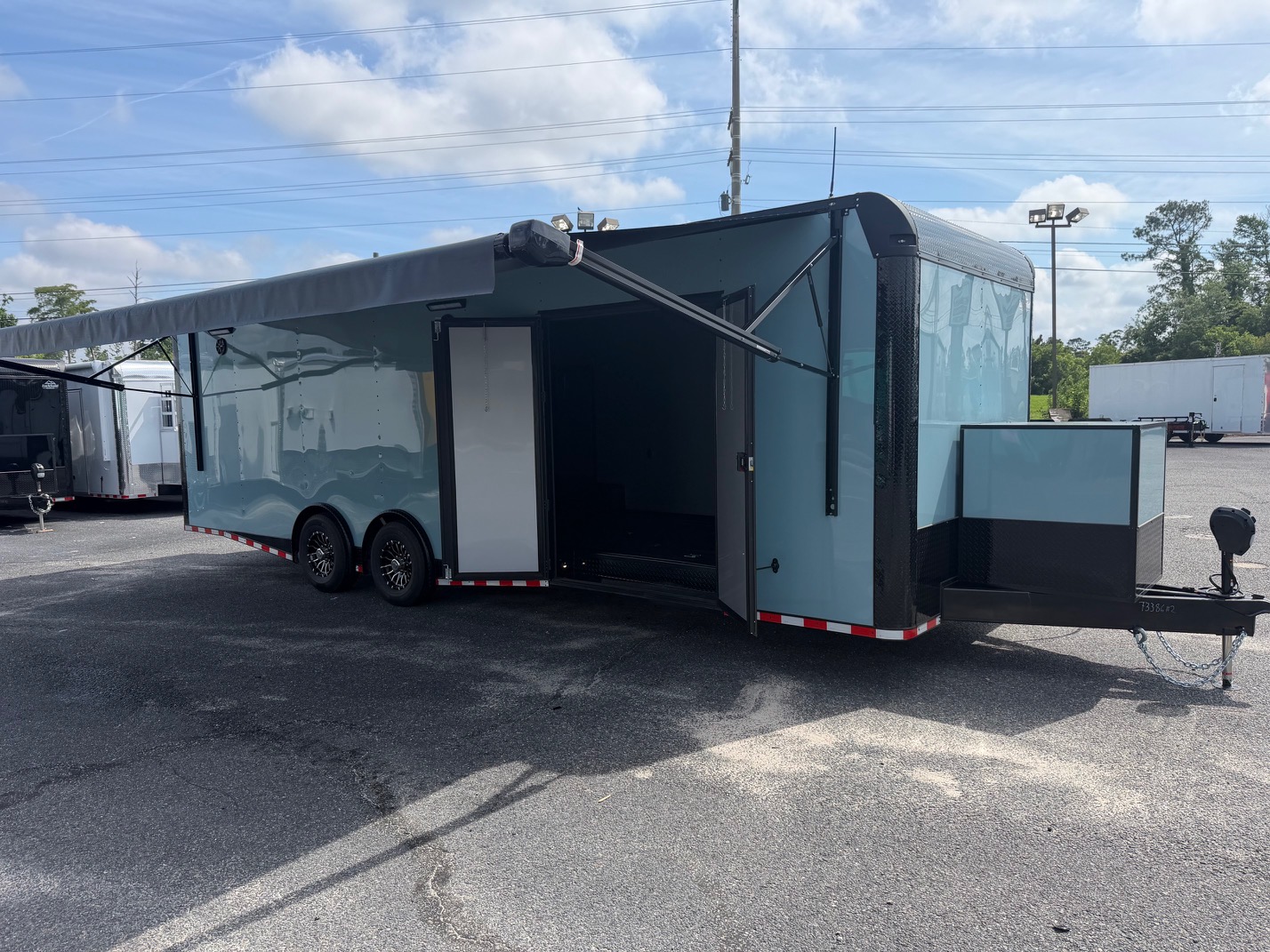 Rock Solid Cargo 8.5x28 enclosed race car trailer in greyish blue with blackout trim, spread torsion axles, electric awning, generator compartment, and custom race package.